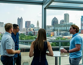 Oliva Gibbs team talking in front of window showing a city skyline