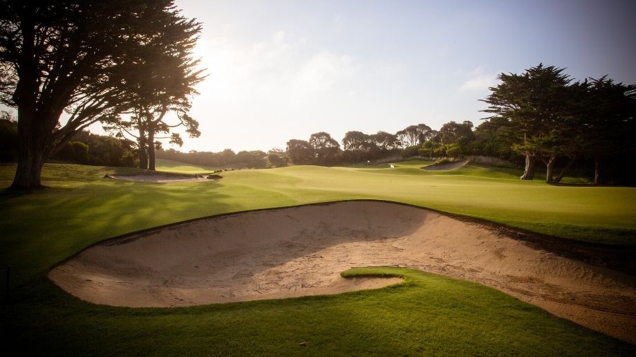 Sand trap on a golf course surrounded by trees at sunset