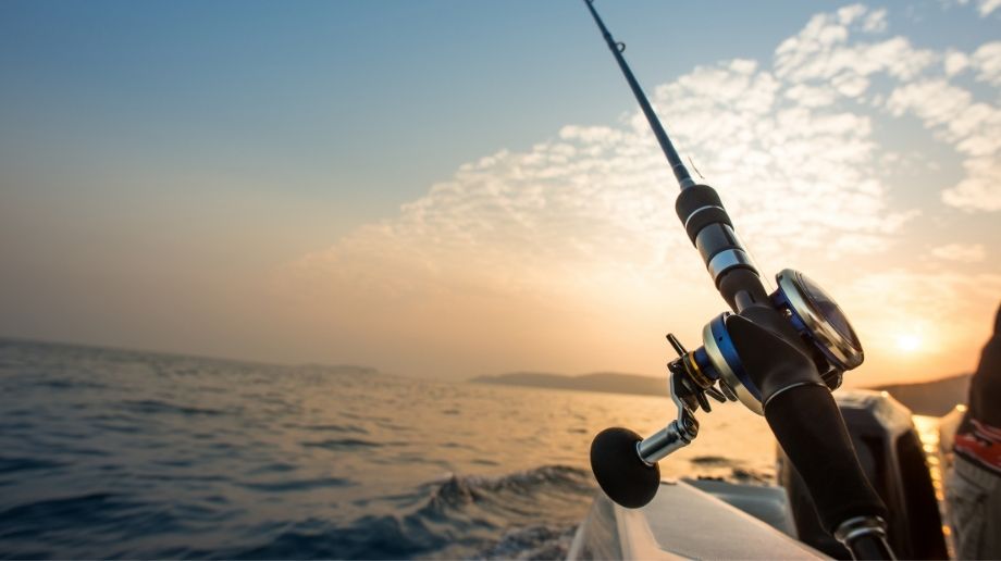 Fishing rod near the hull of a white boat in the ocean at sunset