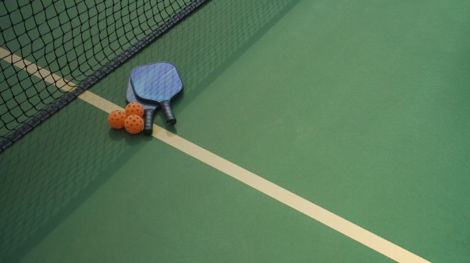 Pickleball paddles and wiffle balls laying on a court