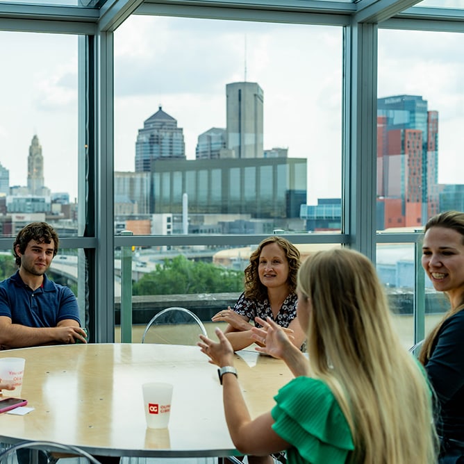 Oliva Gibbs team members meeting at table in front of a glass window showing a city skyline