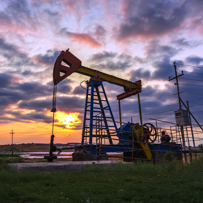 Oil rig pump against a colorful sunset sky